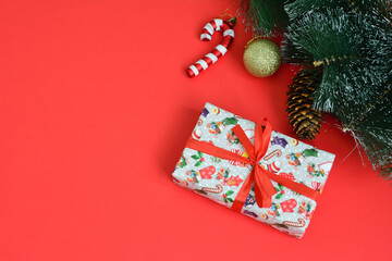 a christmas present with a red ribbon on it and a christmas tree on the background 