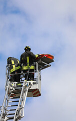 firefighters above the metal basket of the aerial ladder with the stretcher to transport the injured person