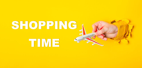 Hand holding a toy airplane with the words shopping time written below it