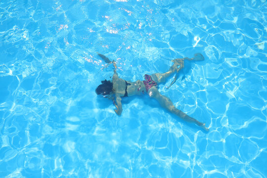 girl lying motionless at the bottom of a blue water pool