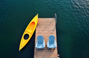 Wooden pier with yellow kayak and two light blue Adirondack chairs. Calm dark teal water surrounds...