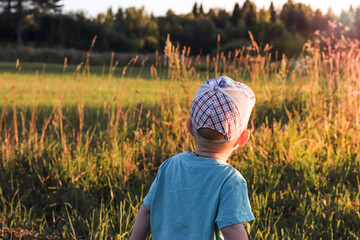 A little boy in a cap looks at the field in sunny weather.