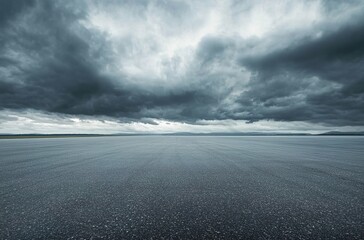  A wide shot of an empty asphalt racetrack with dark gray clouds in the sky.