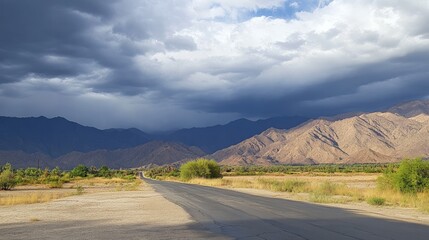 A dramatic view of an asphalt road leading to mountains under stormy clouds.


