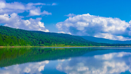 Calm lake reflecting clouds and mountains in bright daylight