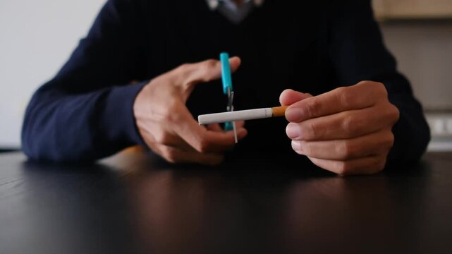  Close-up of hands cutting a cigarette with scissors. Quitting smoking concept.