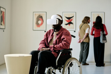 Man in wheelchair experiencing virtual reality headset in modern art gallery, interacting with...
