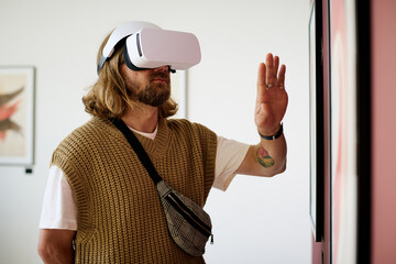 Man immersed in virtual reality experience wearing white headset and interacting with art on wall