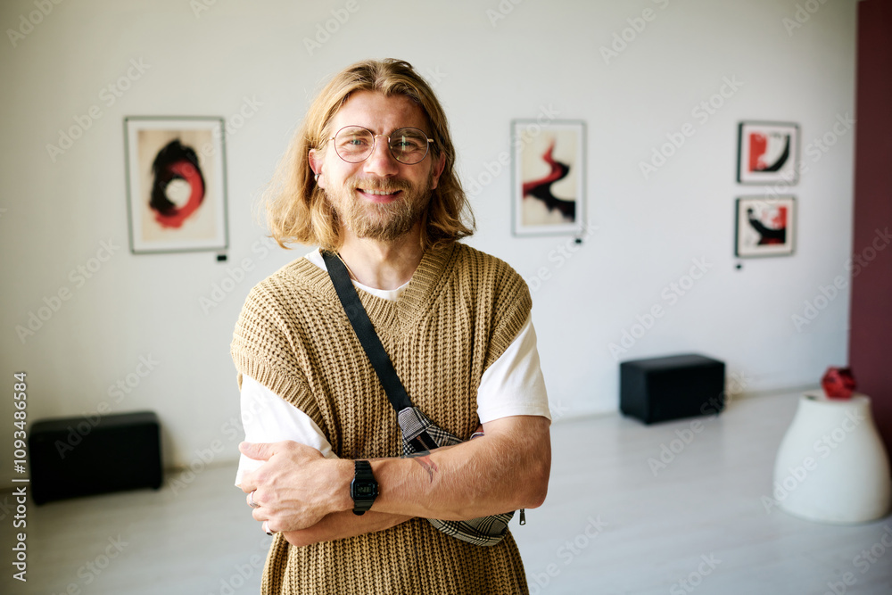 Wall mural Portrait of man with long hair standing in modern art gallery, smiling and wearing casual attire arm crossed and looking directly at the camera