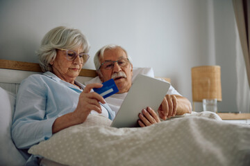 Obraz premium Senior woman using credit card while shopping on internet with her husband.