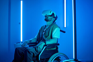 Man in wheelchair experiencing virtual reality with VR headset in high-tech room illuminated by...
