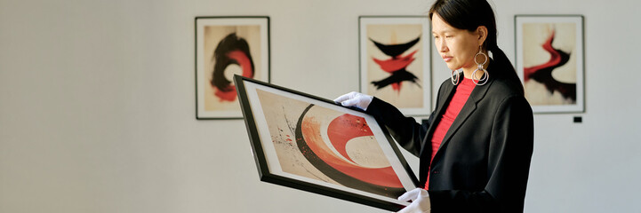 Woman in modern art gallery examining vibrant abstract art while standing with framed artwork in hands, showcasing engagement with contemporary art
