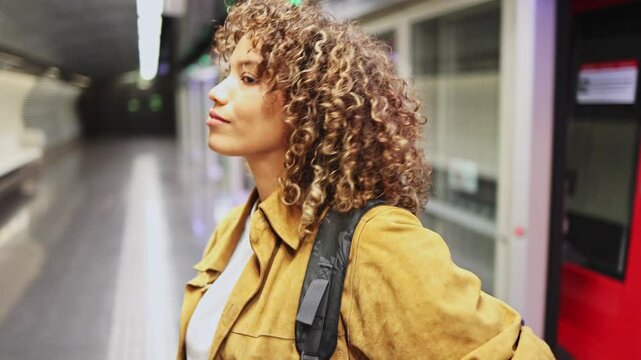 Young latin woman leaving the subway. A young woman with curly hair steps outside the subway car, surrounded by the hustle and bustle of urban life and the expectation