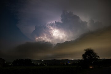 Supercell thunderstorm in the Po Valley, Italy is illuminated by lightning. Blurred tree due to high winds.