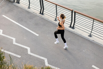 A young woman enjoys a serene morning run along the riverbank promenade, surrounded by modern architecture