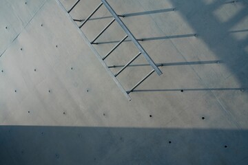 Metal ladder casting shadows on concrete wall.