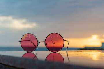 Pink sunglasses with cracked glass lie on the parapet of the promenade against the setting sun. The concept of a day, a year, a life coming to an end with the realization  the discovery of truth.