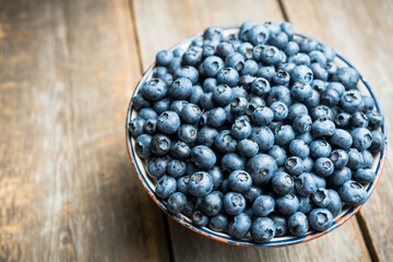 Blueberries in ceramic bowl on rustic wooden background. Selective focus. Shallow depth of field.