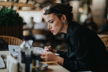 Focused businesswoman intently examining documents at an outdoor cafe table, conveying concentration and professionalism. The ambiance is relaxed yet serious, blending work with a casual atmosphere.