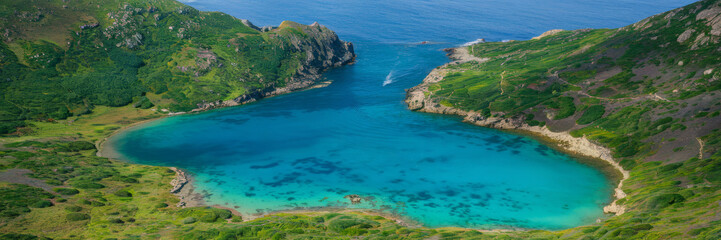 A coastal landscape with a turquoise-blue lake surrounded by green cliffs and rocky ledges. The lake is located in the rocks, creating a secluded natural area with crystal clear shallow water.