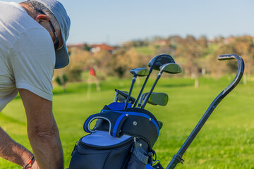 Close-up of senior golfer with cap searching for equipment in golf bag