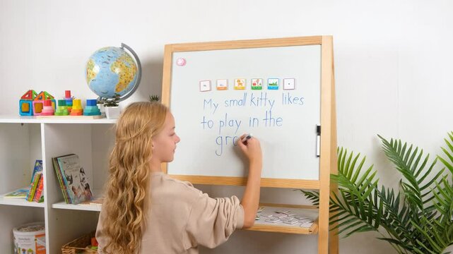 A young girl, a child is having fun learning to build sentences using magnetic word tiles and frames on a whiteboard in a classroom.