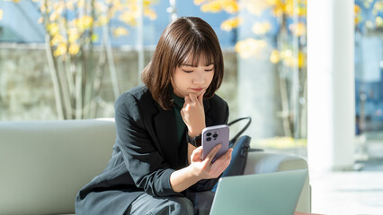 スマホを見て悩む女性・ビジネスウーマン