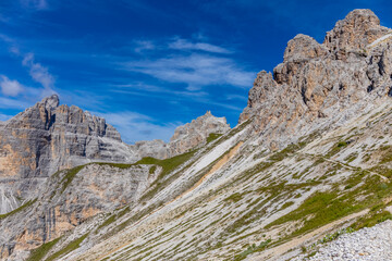 Sunny day in the Dolomites. Rocky mountain peaks of Dolomiti Alps in summer under the blue sky with some clouds prominent mountain summits landscape and stunning views of the alpine range and meadow