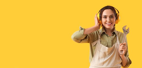 Female worker in hearing protectors and with wrench on yellow background with space for text