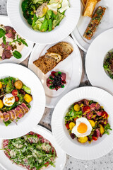 Assorted healthy gourmet dishes on a marble surface, showcasing variety and freshness. Includes vibrant salads, fresh fruits, and artisanal bread, perfect for a balanced diet and culinary inspiration.