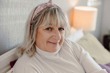 Happy senior woman in white turtleneck sweater smiling indoors relaxed home portrait natural lighting