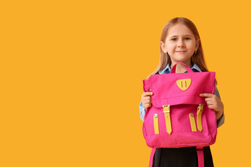 Cute little schoolgirl with backpack on yellow background