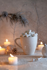 Table with burning candles and a mug of marshmallows is strewn with Christmas snowflakes Close-up.