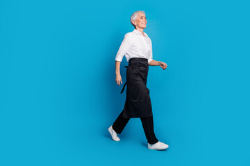 Full length photo of lovely pensioner lady walking serve clients coffee shop dressed waitress uniform isolated on blue color background