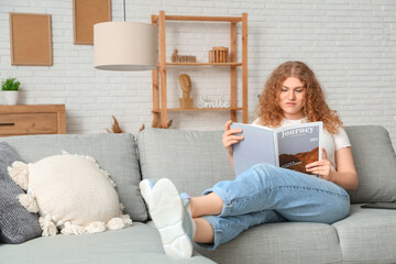 Young woman reading magazine on sofa at home