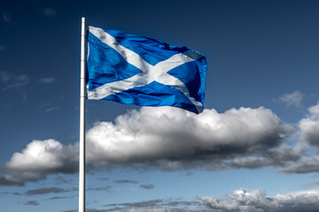 Flag Of Scotland (Saltire or St. Andrew`s Cross) Flutters In The Wind In Front of Blue Sky And Clouds
