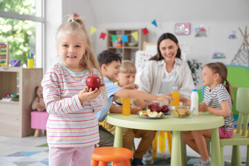 Cute little girl with apple having lunch in kindergarten