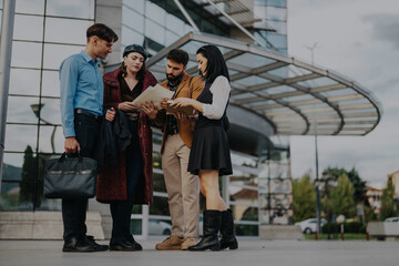 A group of business professionals stand outside a sleek, modern office building reviewing documents. The image captures teamwork, collaboration, and a professional setting in a contemporary urban