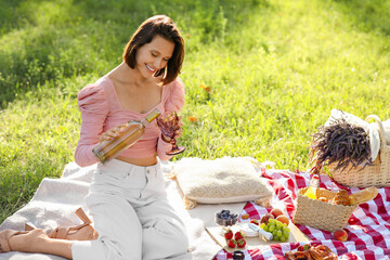 Beautiful young woman pouring wine into glass at picnic in park