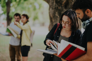 Students gather around a professor in a park setting, engaging in academic discussion and sharing...