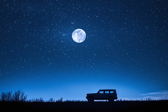 A single vehicle's silhouette against a vast, starry sky, full moon.