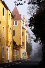 Old yellow building with a spire and an attic on a quiet narrow street. Austria