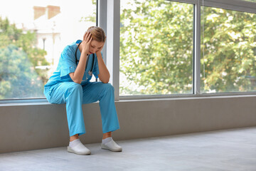 Tired female doctor with stethoscope sitting near window in clinic