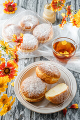 Yummy set of cake donuts with vanilla, custard, powdered sugar on plate on wooden background with cup of tea and flowers. Sweets, dessert and pastry, close up
