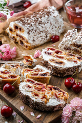 Pieces of delicious Monastic hut cake with cherry filling, cream and chocolate on wooden background with cup of tea and rose flowers. Holiday dessert, sweets and pastry, close up