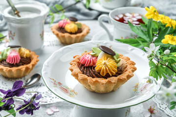 Delicious mini basket cakes or sand tartlets cake with cream on plate over light background with flowers and cup of tea. Sweets, dessert and pastry, close up