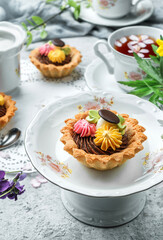 Delicious mini basket cakes or sand tartlets cake with cream on plate over light background with flowers and cup of tea. Sweets, dessert and pastry, top view, selective focus