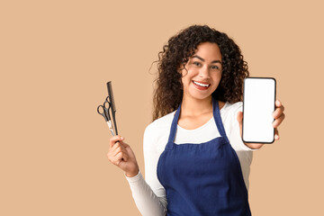Beautiful young happy African-American hairdresser with mobile phone, scissors and comb on beige background