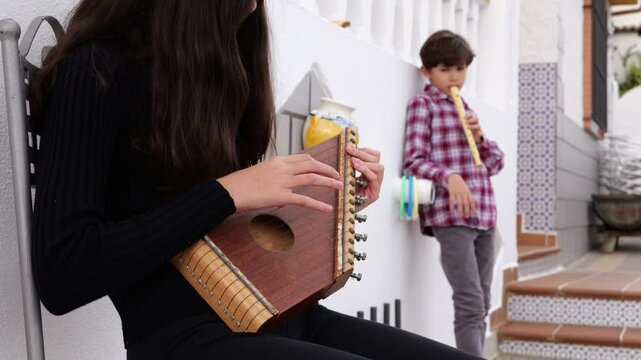 Girl Playing Zither While Her Brother Plays Flute in Their Home Patio, Learning