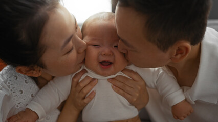 Parents lovingly kiss their cheerful baby in a cozy home setting showcasing family love and tenderness.